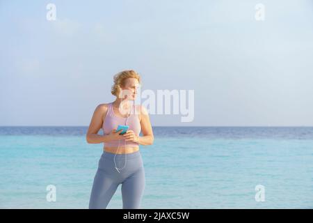 Eine sportliche Frau hört am Strand auf ihrem Smartphone Musik. Stockfoto