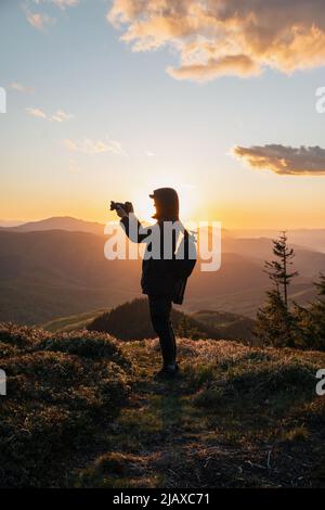 Silhouette des Menschen, der die Kamera beim Sonnenuntergang auf dem Berg hält Stockfoto