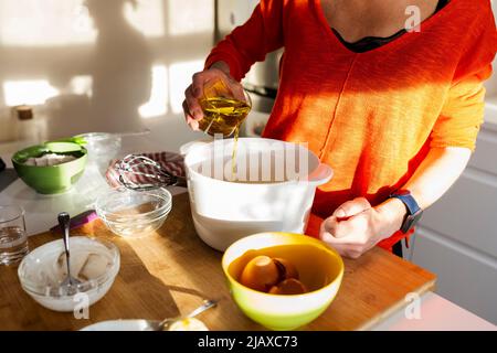 Frau gießt Öl in eine Schüssel in der Küche. Stockfoto