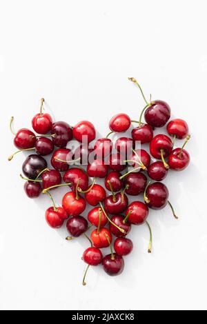 Rote Kirschen in Herzform auf weißem Holz Stockfoto