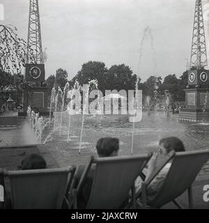 1953, historisch, Battersea Park, London, Menschen sticht in Liegestühlen neben dem Brunnensee in den Festival Pleasure Gardens, zum Zeitpunkt der Feierlichkeiten zur Krönung der Königin. Der Wassergarten und die Springbrunnen wurden 1951 im Rahmen des Festivals von Großbritannien errichtet, als der Park in Battersea Pleasure Gardens umgewandelt wurde, als auch eine Vergnügungsmesse gebaut wurde. Stockfoto