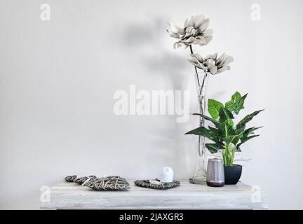 Eingetopftes grünes natürliches und graues Kunstblumen in Vase mit niedlichen Wohnaccessoires auf Tisch über weißem Wandhintergrund, Kopierraum Interieur Stockfoto