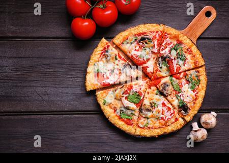 Gesunde, glutenfreie Blumenkohlkruste Pizza mit Tomaten, Pilzen und Spinat. Draufsicht mit geschnittenen Slices. Tischszene auf dunklem Holz Stockfoto