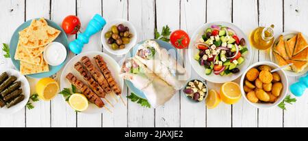 Griechische Essenstischszene, Draufsicht auf weißem Holz-Banner-Hintergrund. Auswahl an Artikeln wie Gyros Wraps, Souvlaki, Salat, Spanakopita, Dolmades, pi Stockfoto