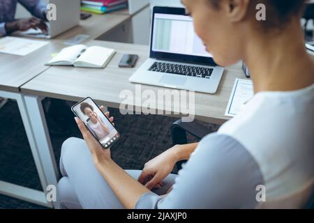 afroamerikanische junge Kolleginnen, die im Büro über ein Smartphone per Videoanruf telefonieren Stockfoto