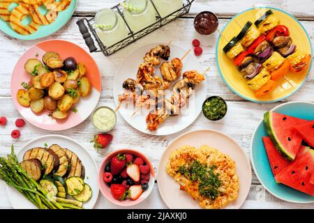 Veganes sommergrillen oder Picknick-Tischszene. Blick von oben auf einem weißen Holzhintergrund. Obst, gegrilltes Gemüse, Spieße, Blumenkohlsteak und Limonade. Stockfoto