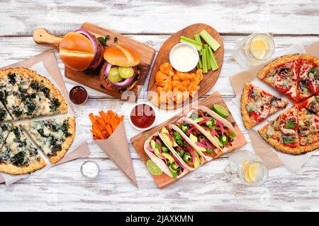 Gesunde Pflanze basiert Fast-Food-Tabelle Szene. Draufsicht auf weißem Holzhintergrund. Pizzas aus Blumenkohlkruste, Bohnenburger, Pilztacos, Paprika na Stockfoto