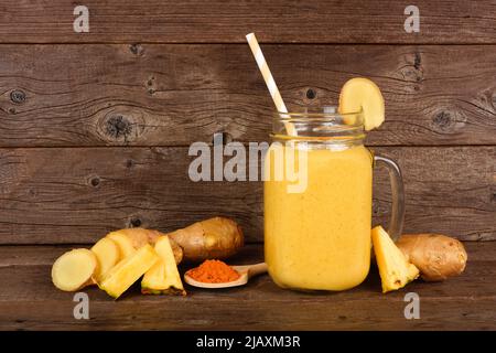 Ananas, Kurkuma, Ingwer-Smoothie in einem Einmachglas vor dunklem Holz mit Zutaten. Gesunde Immunantwort, Gewichtsverlust, Anti-Inflam Stockfoto