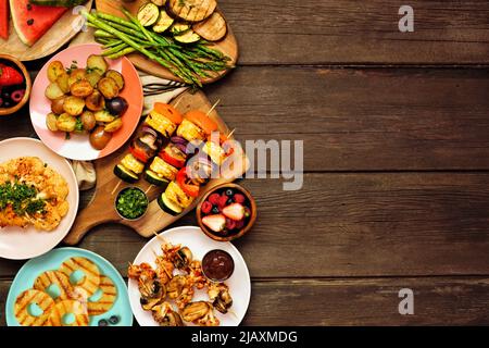 Veganes Sommer-bbq oder Picknick am Rand. Blick über einen dunklen Holzhintergrund. Gegrilltes Obst und Gemüse, Spieße, Blumenkohlsteak und Vegetaria Stockfoto