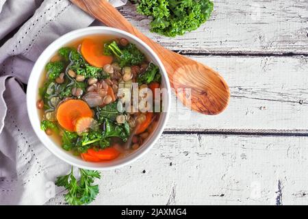 Gesunde Gemüsesuppe mit Grünkohl und Linsen. Deckenansicht Tischszene auf einem rustikalen weißen Holzhintergrund. Stockfoto