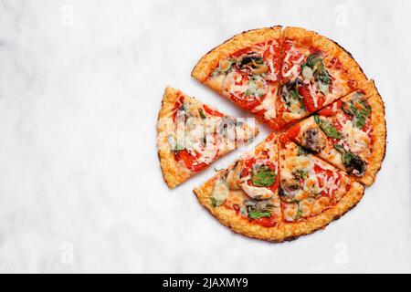 Gesunde, glutenfreie Blumenkohlkruste Pizza mit Tomaten, Pilzen und Spinat. Draufsicht mit geschnittenen Scheiben auf weißem Marmorhintergrund. Stockfoto