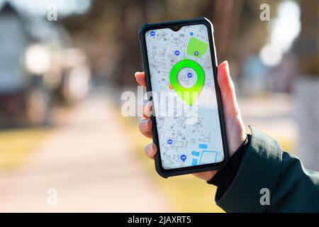 Die Hand einer Frau hält ein Mobiltelefon bei geöffneter Online-Karten-App und zeigt den markierten Ort auf der Karte an. Nahaufnahme. Das Konzept der Online-Navigatoren. Stockfoto