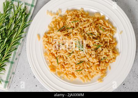 Reispilaf mit Orzo, serviert mit frischem Rosmarin, Nahaufnahme auf weißem Teller, flach legen Stockfoto