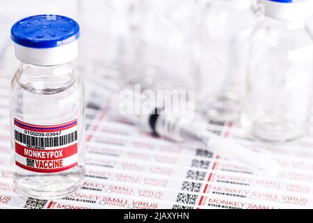 Ampulle oder Fläschchen mit Monkeypox-Virus-Impfstoff mit Gefahrenetiketten und Warnhinweisen im Hintergrund Stockfoto