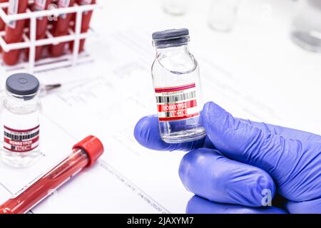 Hand des Apothekers mit Ampulle oder Fläschchen mit Monkeypox-Impfstoff, Röhrchen mit kontaminiertem Blut im Hintergrund Stockfoto