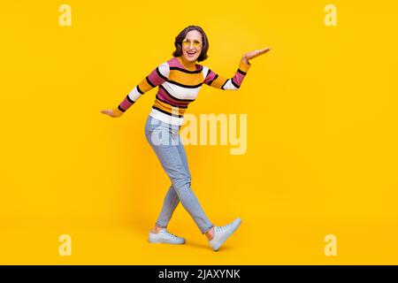 In voller Länge Foto von kühlen grauen Frisur im Alter Dame Tanz tragen Brillen Pullover Jeans Schuhe auf gelbem Hintergrund isoliert Stockfoto