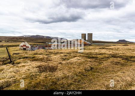 Eine verlassene Industrie ruin mit zwei hohen Betonsilos verfällt an den Ufern des Gígvatnsvatn auf der Reykjanes-Halbinsel in Island. Die Gebäude sind jetzt stark mit Graffiti bedeckt, darunter das Wort ‚TRASHR‘. Stockfoto