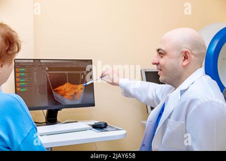 Ein männlicher Augenarzt erklärt einer erwachsenen Frau die Ergebnisse einer Augenuntersuchung und zeigt eine Zeichnung auf einem Computer. Stockfoto