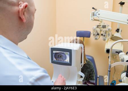 Ein männlicher Augenarzt überprüft das Augenlicht eines jungen Mädchens mit einem modernen Sehgerät. Stockfoto