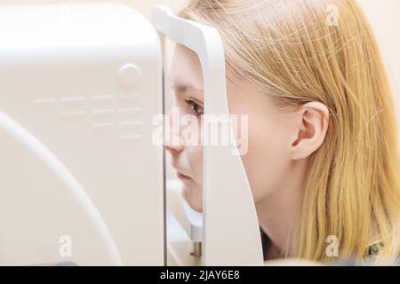 Ein junges Mädchen an der Rezeption des Augenarztes überprüft ihr Sehvermögen an einem speziellen Apparat. Nahaufnahme. Stockfoto