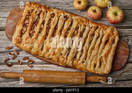 Hausgemachter Apfel- und Walnusskuchen auf einem Holzbrett, umgeben von Zutaten, auf einem rauen Holztisch. Essen zu Hause Stockfoto