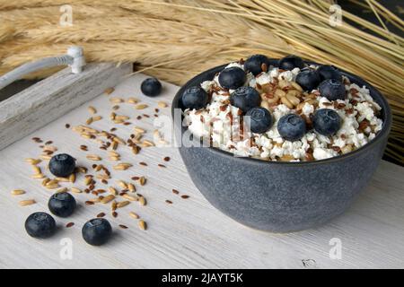 Vollkorn-Haferflocken mit Heidelbeeren, Leinsamen und Quark auf einem vintage gefärbten Regal, umgeben von einer Garbe von Ohren Stockfoto