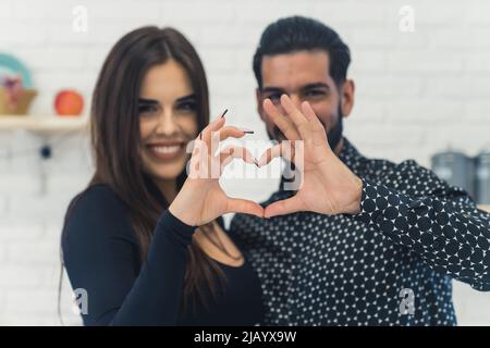 Ein nettes Paar, das eine Herzgeste zur Kamera macht. Hochwertige Fotos Stockfoto