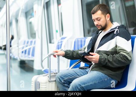 Männlicher Passagier in legerer Kleidung, der in der U-Bahn über das Mobiltelefon spricht Stockfoto