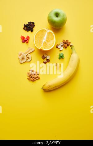 Hohe Winkelansicht des Querschnitts von Orange, Apfel, Banane, frittierten Früchten und Nüssen auf gelbem Hintergrund Stockfoto