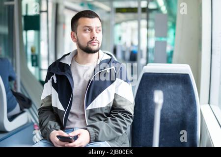 Bärtiger Mann, der im Stadtbus unterwegs war und ein Handy benutzte Stockfoto