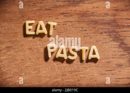 Text Eat Pasta gebildet mit Alphabet Suppe Pasta Buchstaben auf einem hölzernen Hintergrund. Konzept: Italienisches Essen Stockfoto