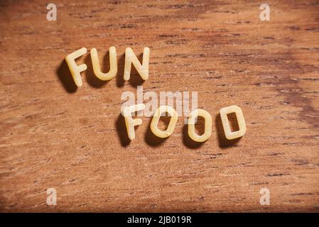 Text Fun Food mit Alphabet Suppe Pasta Buchstaben auf einem hölzernen Hintergrund gebildet. Stockfoto