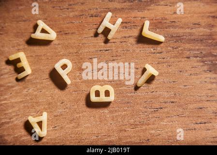 Buchstaben des Alphabets Wort aus Suppenteigwaren in Unordnung auf einer hölzernen Oberfläche gelegt gemacht Stockfoto