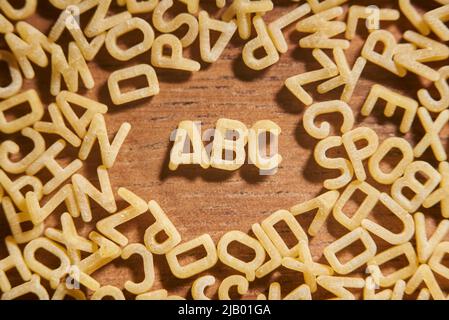 Alphabet Suppe Pasta Buchstaben, ABC umgeben von einem Rahmen von Buchstaben in Unordnung, auf einem hölzernen Hintergrund. Konzepte von Nahrung und Bildung. Stockfoto