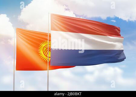 Sonniger blauer Himmel und Flaggen der niederlande und kirgisistans Stockfoto