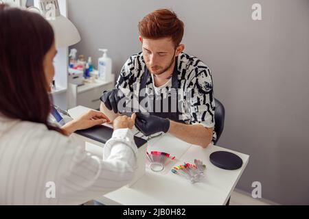 Junger Nagelmeister, der mit dem Kunden im Schönheitssalon arbeitet Stockfoto