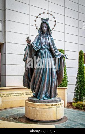 2022 04-21 Tulsa USA - Mary Queen of Heaven Statue auf rundem Sockel vor dem St. Francis Hospital, teilweise umgeben von Felswänden und Zypressen Stockfoto