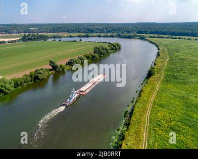 Kleines Schleppboot schiebt Barge entlang ruhigem Wasser vorbei an Feldern Stockfoto