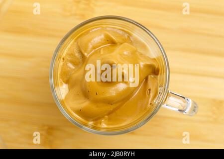 Den Dalgona-Kaffee in einem durchsichtigen Kaffeebecher peitschten. Koreanisches Getränkekonzept. Selektiver Fokus Stockfoto