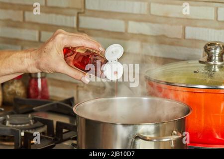 Ahornsirup wird nach Rezept aus dem Internet auf dem Gasherd in einen Topf gegossen. Dampftopf. Stockfoto