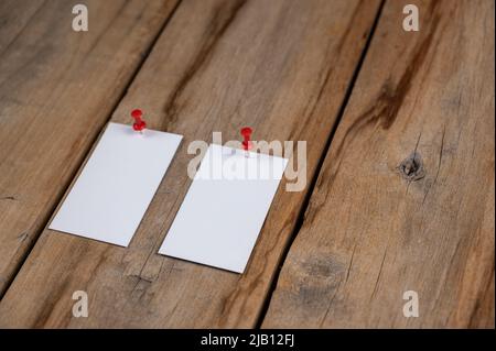 Zwei leere Visitenkarten vor einem hölzernen Hintergrund. Rechtecke aus weißem Papier, die mit Stecknadeln an alten Brettern befestigt sind. Selektiver Fokus. Stockfoto