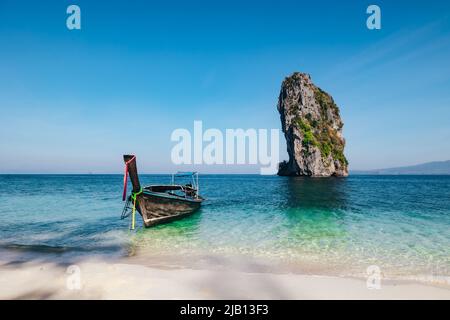 Ein Longtail-Boot vor Anker auf einem weißen Sandstrand auf Ko Poda Island während des Morgens mit tropischem, blau türkisfarbenem Wasser und Kalksteinfelsen in Krabi Thailand Stockfoto