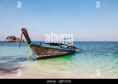 Ein Longtail-Boot vor Anker auf einem weißen Sandstrand auf Ko Poda Island während des Morgens mit tropischem, blau türkisfarbenem Wasser und Kalksteinfelsen in Krabi Thailand Stockfoto
