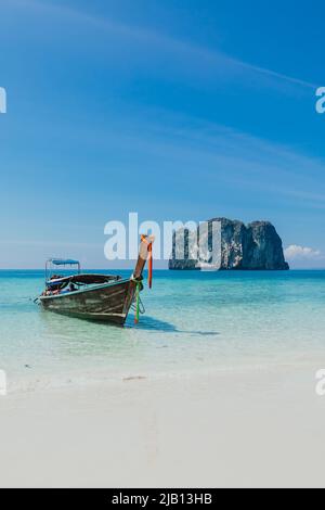 Ein Longtail-Boot vor Anker auf einem weißen Sandstrand auf Ko Poda Island während des Morgens mit tropischem, blau türkisfarbenem Wasser und Kalksteinfelsen in Krabi Thailand Stockfoto