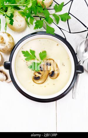 Suppenpüree aus Champignons, Kartoffeln, Zwiebeln und Rahm in einer Schüssel, Serviette, Petersilie und Löffel auf Holzbrett Hintergrund von oben Stockfoto