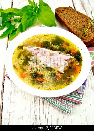 Schweinebrippen-Suppe mit Couscous und Spinat auf einem Teller auf einer Serviette, Brot auf dem Hintergrund eines hellen Holzbretts Stockfoto