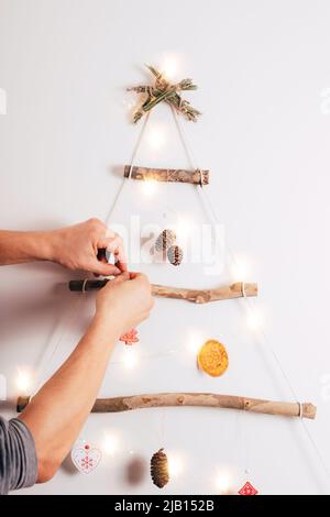 Männerhände schmücken Weihnachtsbaum aus trockenen Sticks, trocken orange, Zapfen auf weißem Hintergrund. Zero Waste Weihnachten, Neujahr, umweltfreundliche concep Stockfoto