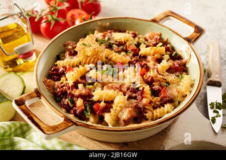 Hoher Winkel von gebackenen appetitlichen italienischen Fusilli Pasta mit Hackfleisch Kräuter und Tomaten auf Holz Schneidebrett mit Öl und gehackten Zucchini Stockfoto