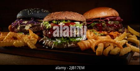 Leckere Hamburger mit Koteletts und Gemüse auf Schneidebrett mit Pommes Frites im Studio serviert Stockfoto