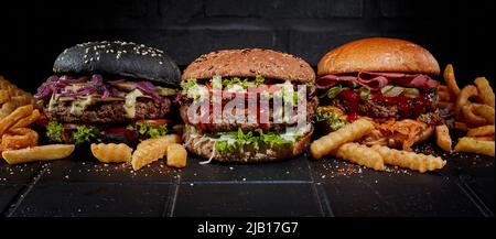 Leckere Hamburger und Pommes frites werden auf dem Tisch im Studio auf dunklem Hintergrund serviert Stockfoto